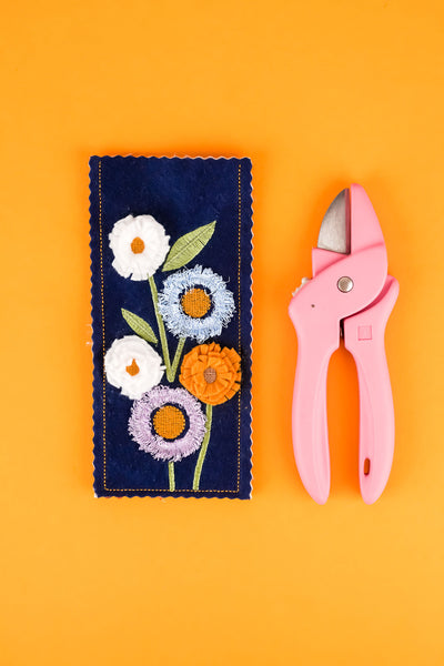 Stickmotiv Blumen für das Etui für Blumenschere in blau mit einer rosafarbenen Schere rechts daneben zum Größenvergleich