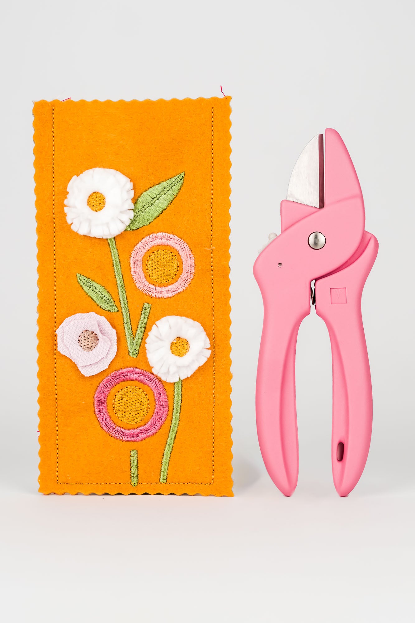 Stickmotiv Blumen für das Etui für Blumenschere in senffarben mit einer rosafarbenen Schere rechts daneben zum Größenvergleich