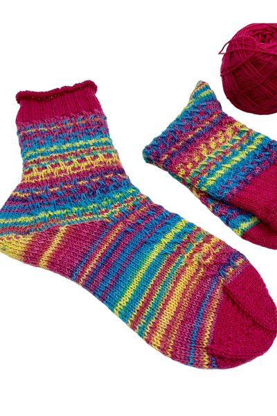 Colourful 15-Years-Socks in gradient yarn beside a matching ball of yarn
