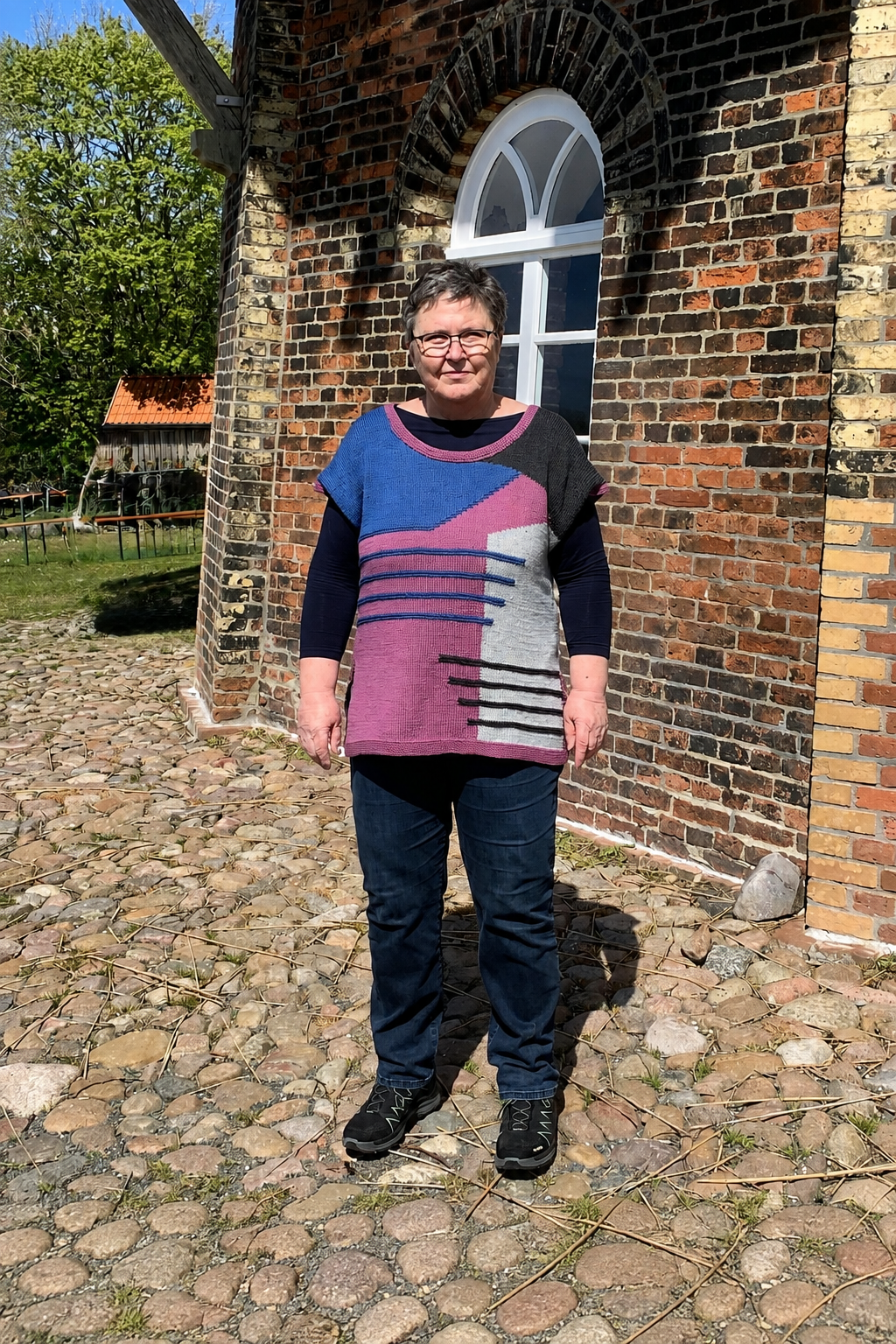 Der Intarsia Magic Slipover als ärmelloser Pullunder über einem dunklen Oberteil.