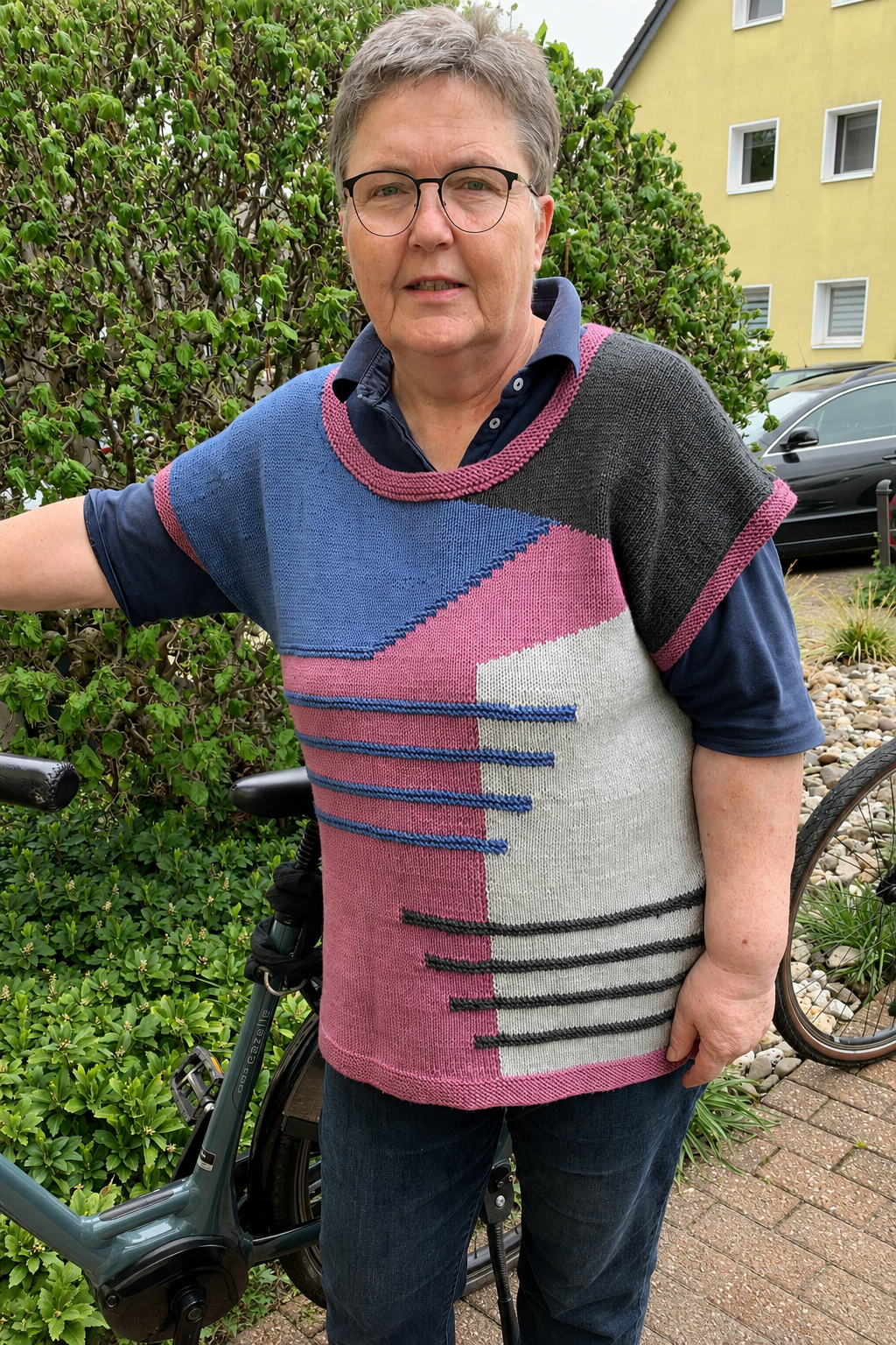 Eine Person trägt den Intarsia Magic Slipover in Blau, Rosa, Hellgrau und Anthrazit.